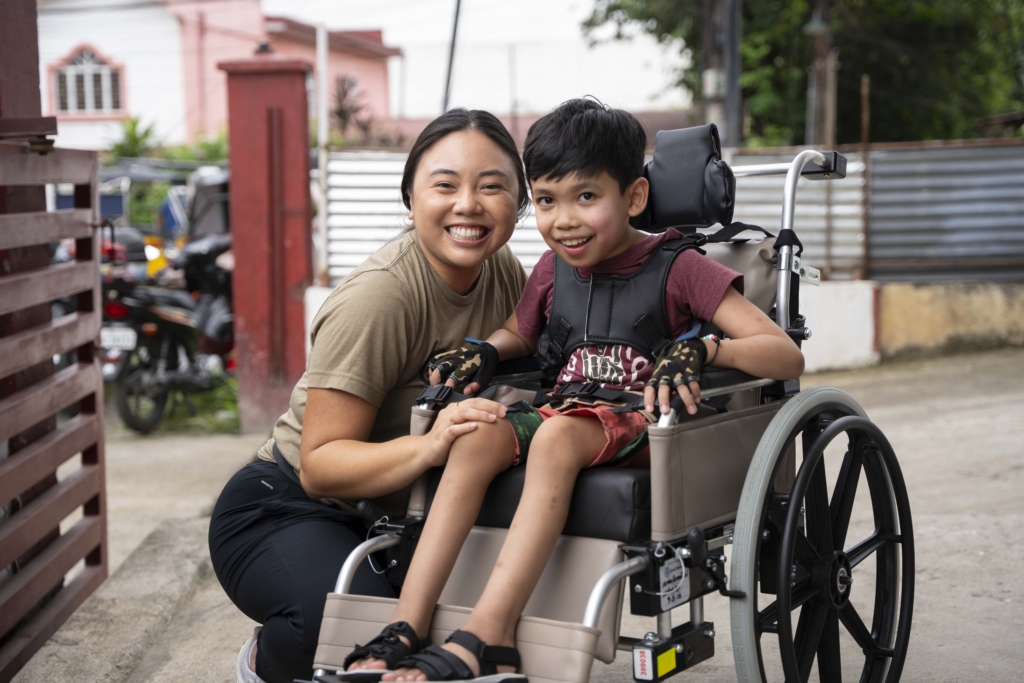 A staff member from Joni and Friends and a boy in his new wheelchair are both smiling and posing joyfully for the camera.