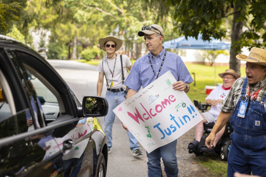 Mark holds a colorful banner that reads "Joni and Friends Family Retreat: Welcome Back, Justine!!"
