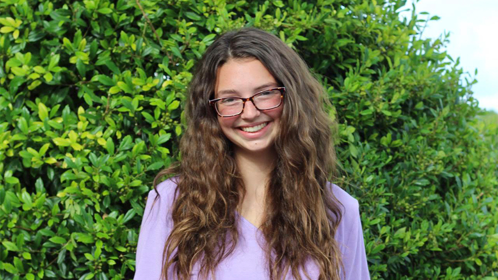 Heidi Swartley smiling at the camera with tall green plants in the background.