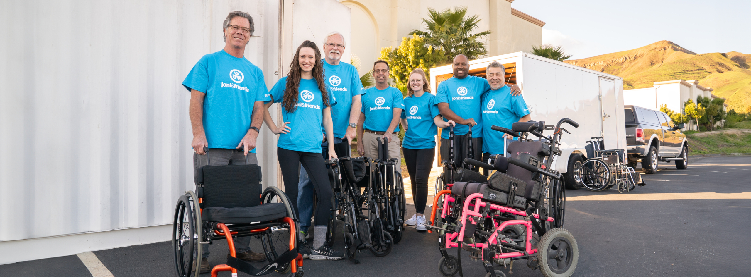 A group of smiling Joni and Friends volunteers poses for a photo, grouped around wheelchairs that have been generously donated.