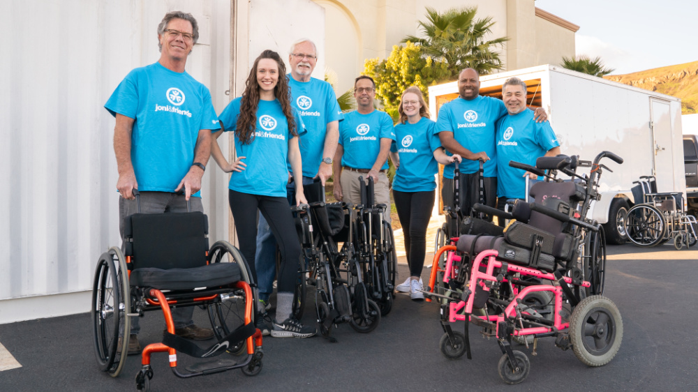 A group of smiling Joni and Friends volunteers poses for a photo, grouped around wheelchairs that have been generously donated.