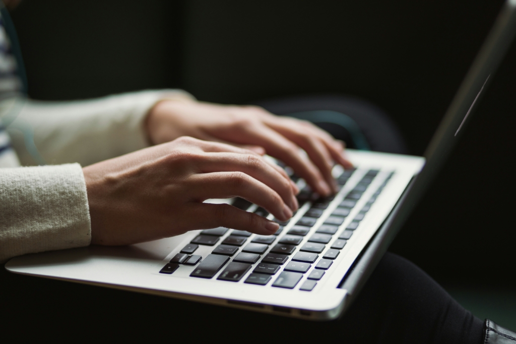 A close-up of two hands typing on a silver laptop, with a blurred background.