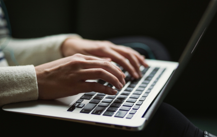 A close-up of two hands typing on a silver laptop, with a blurred background.