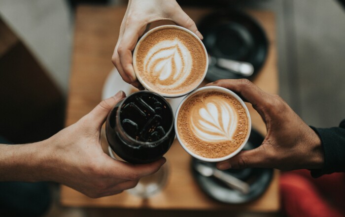 A picture from above three people's hands "cheersing" their coffee drinks.