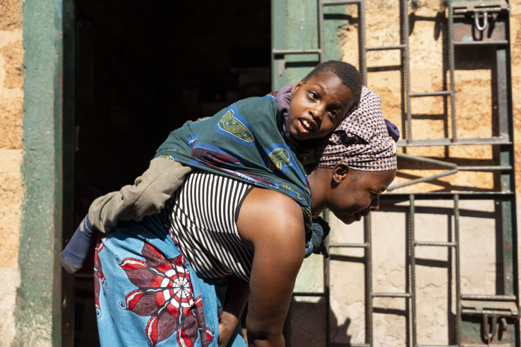 Chisomo is nestled on his mother's back, wrapped in a green cloth. 