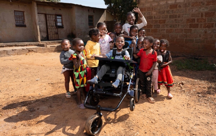 Chisomo, with a huge bright smile, sits in his new cub chair surrounded by happy children celebrating their friend. The picture conveys feelings of happiness, joy, and hope.