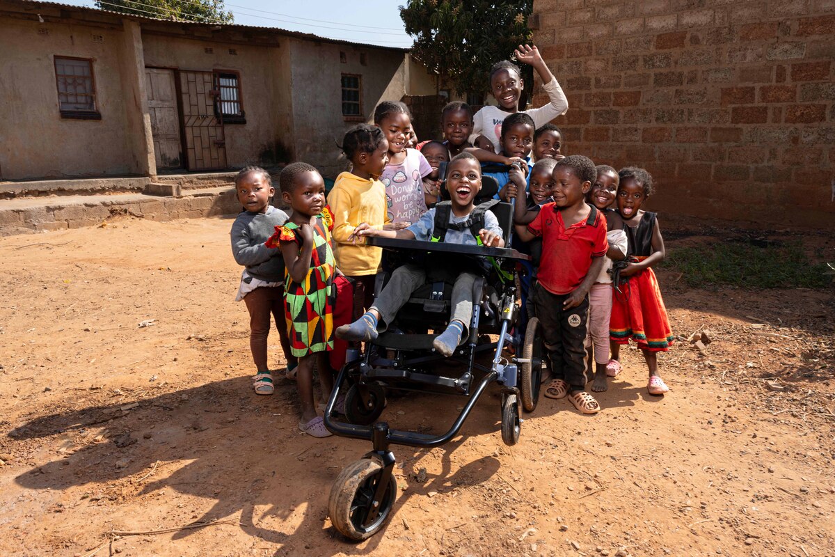 Chisomo, with a huge bright smile, sits in his new cub chair surrounded by happy children celebrating their friend. The picture conveys feelings of happiness, joy, and hope.