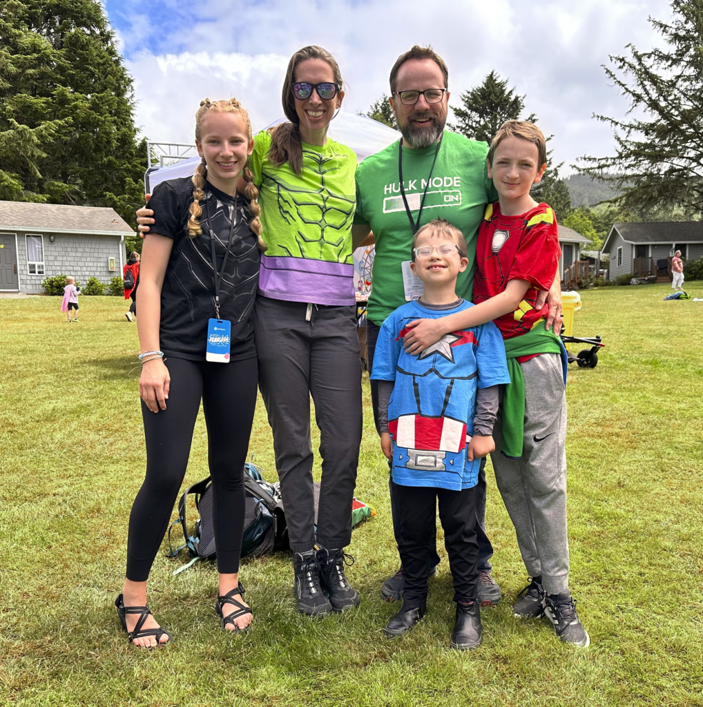 A family picture of Colton, where everyone is wearing their favorite superhero t-shirts, standing together on the grass.