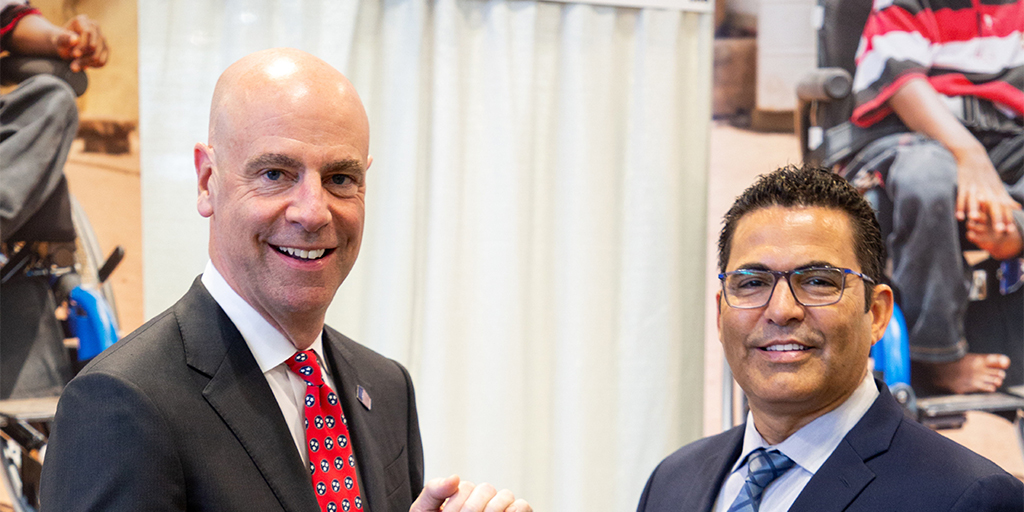 Damon T. Hininger, President and CEO of CoreCivic, and Paul Dorthalina, Director of Wheels for the World at Joni and Friends, are smiling and posing for the camera while holding an award together.