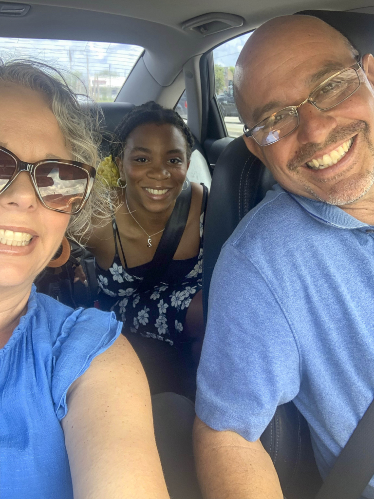 Sara Pueblo on the left, Esther at the back of the car, and David in the driver's seat, all smiling and posing for the camera.