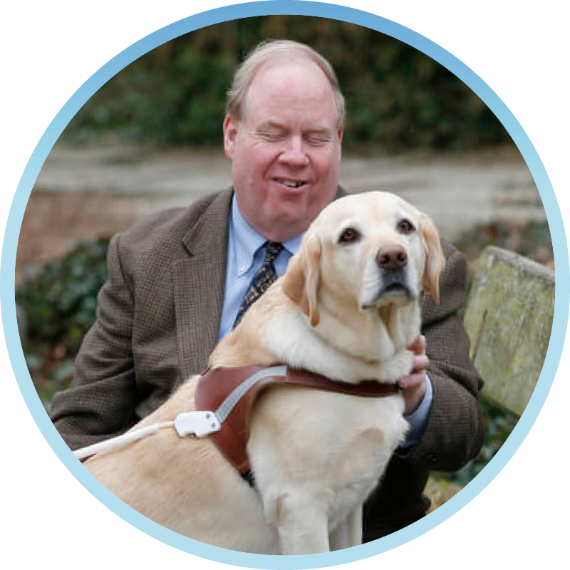 Michael Hingson sits on a park bench with his guide dog, Roselle, in a circular frame with a blue border.