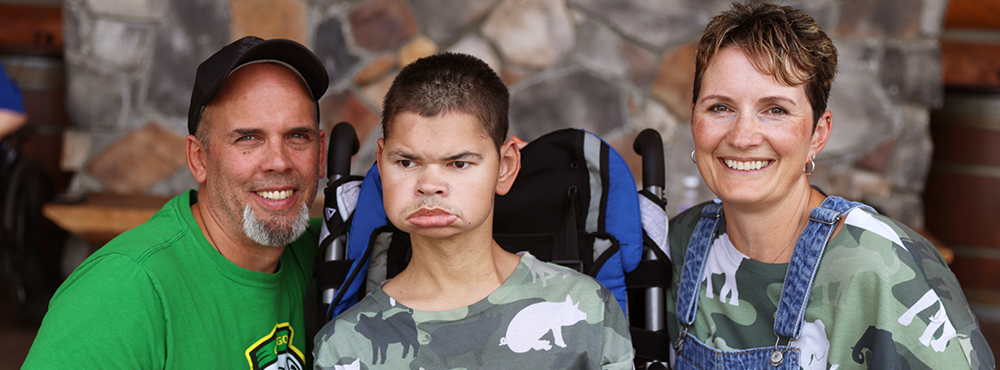 A man on the left, a boy in a wheelchair in the center, and a woman on the right, all smiling for the camera.