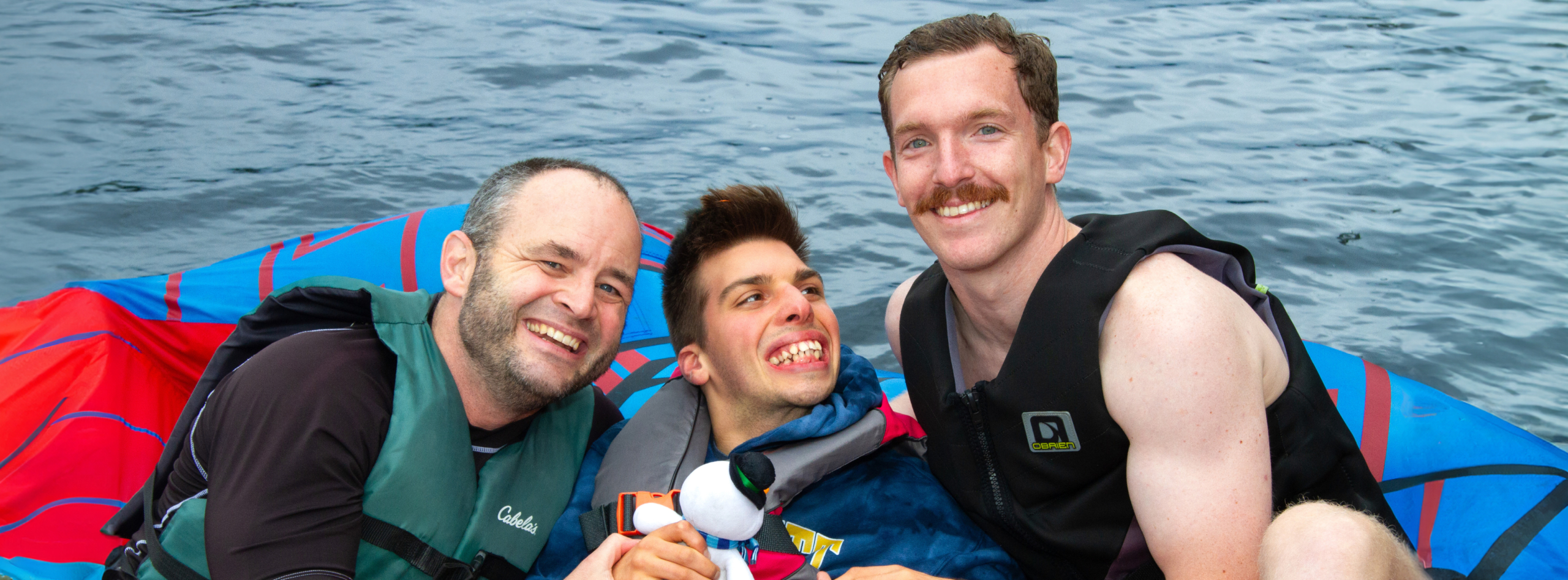 Three men wearing life vests smile for the camera with water surrounding them.