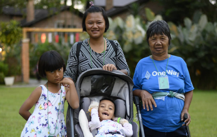 Yupin behind Air in her stroller, with Praewa on the left and another woman with a cane, all smiling and posing for the camera in a grassy area with a slightly blurry background.