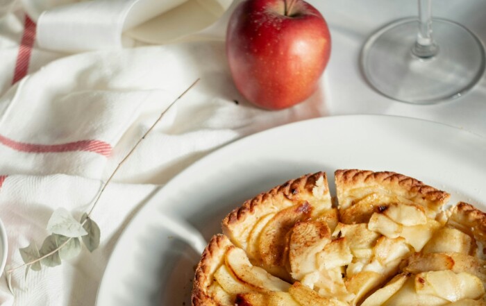 A picture of an apple pie with an apple beside it on a table with a white tablecloth.