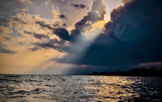 A picture of the ocean with the sun shining on it through a dark cloud above.