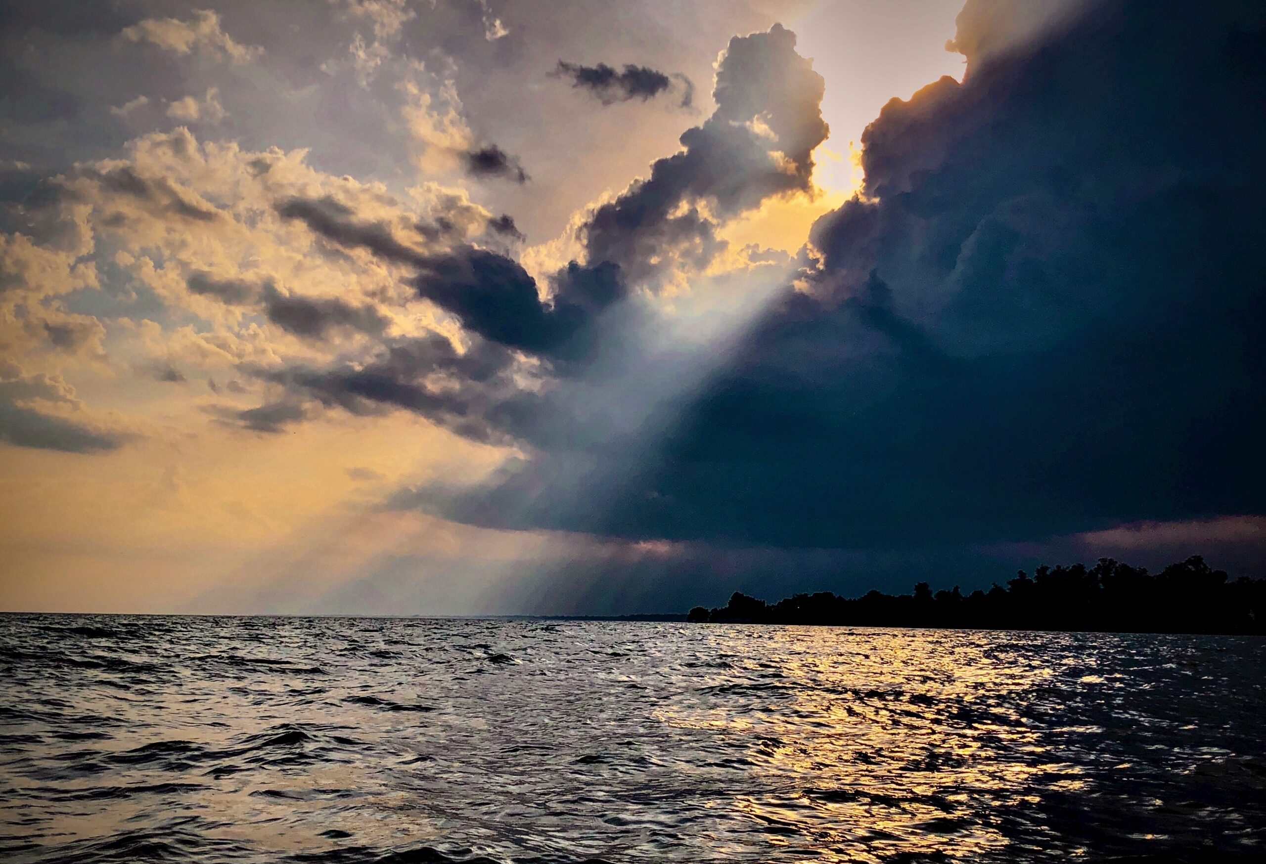 A picture of the ocean with the sun shining on it through a dark cloud above.