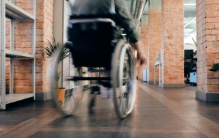 A person in a wheelchair seen from behind, pushing themselves down a hallway.