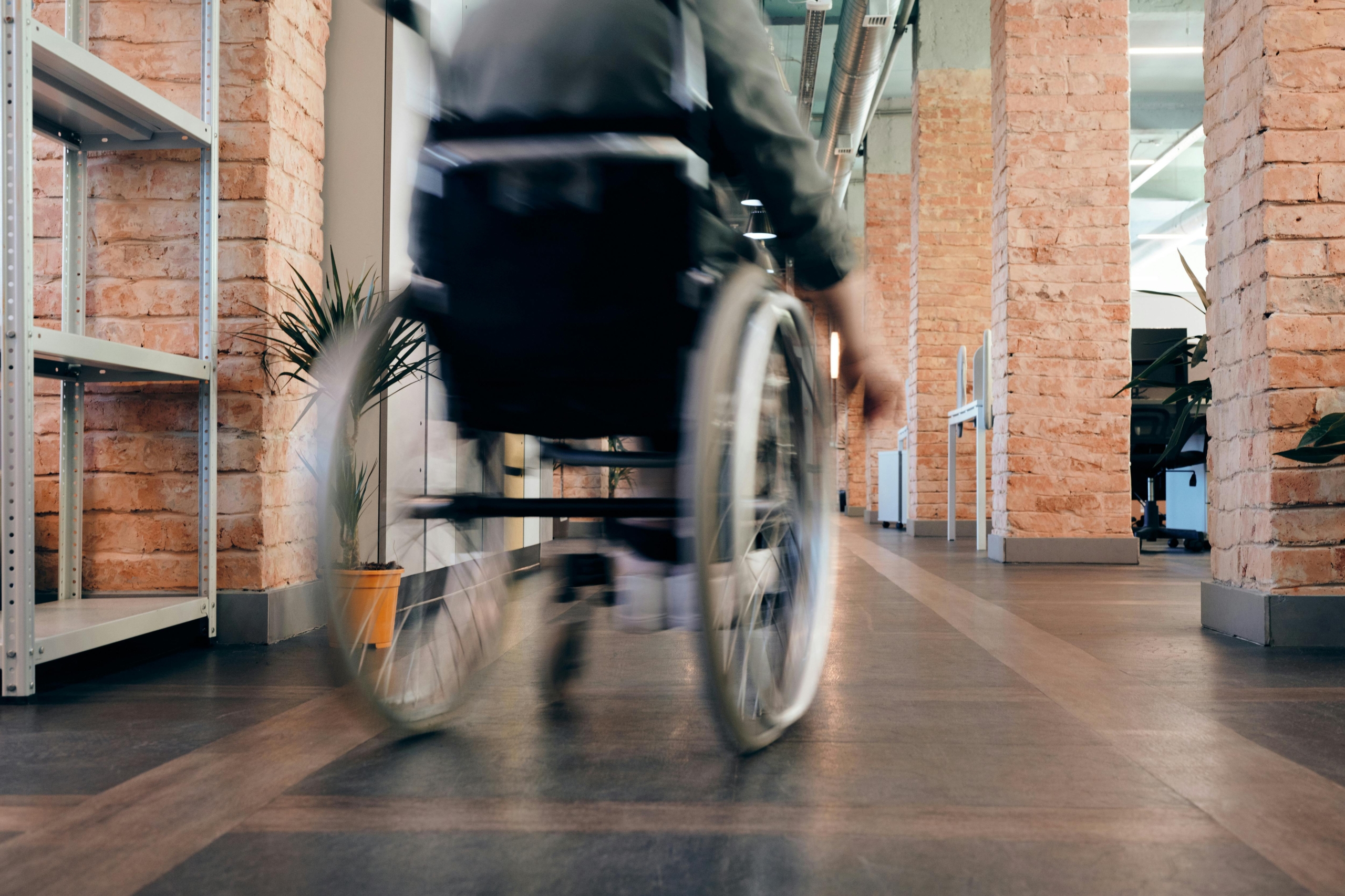 A person in a wheelchair seen from behind, pushing themselves down a hallway.