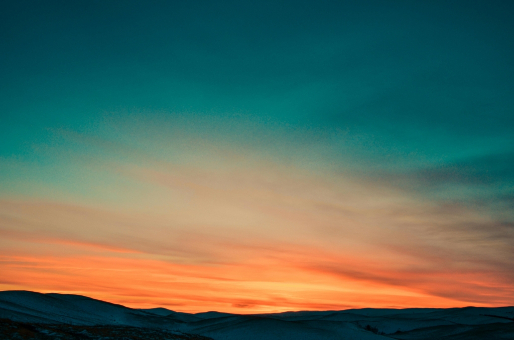 A picture of the sky showcasing various hues of blue, yellow, and orange, with a mountain silhouette at the bottom.