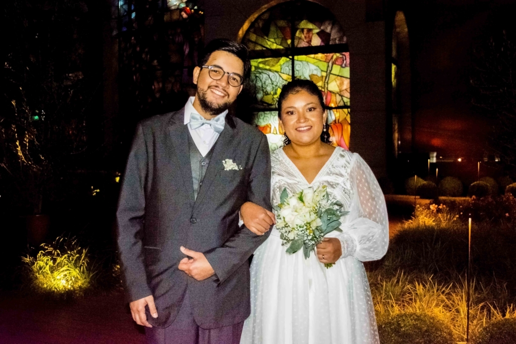 Andrew wearing a tuxedo and Alba wearing a white gown, holding a bouquet of white flowers. They are posing and smiling for the camera, with Alba holding Andrew's arm for their wedding picture.