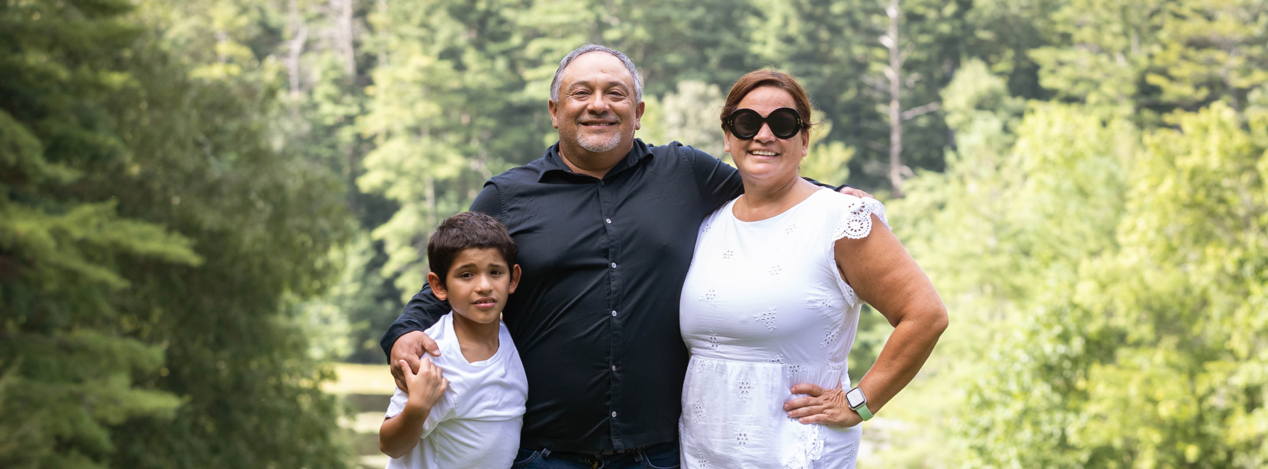 A smiling family poses in the woods as they enjoy rest and fun at Family Retreat.