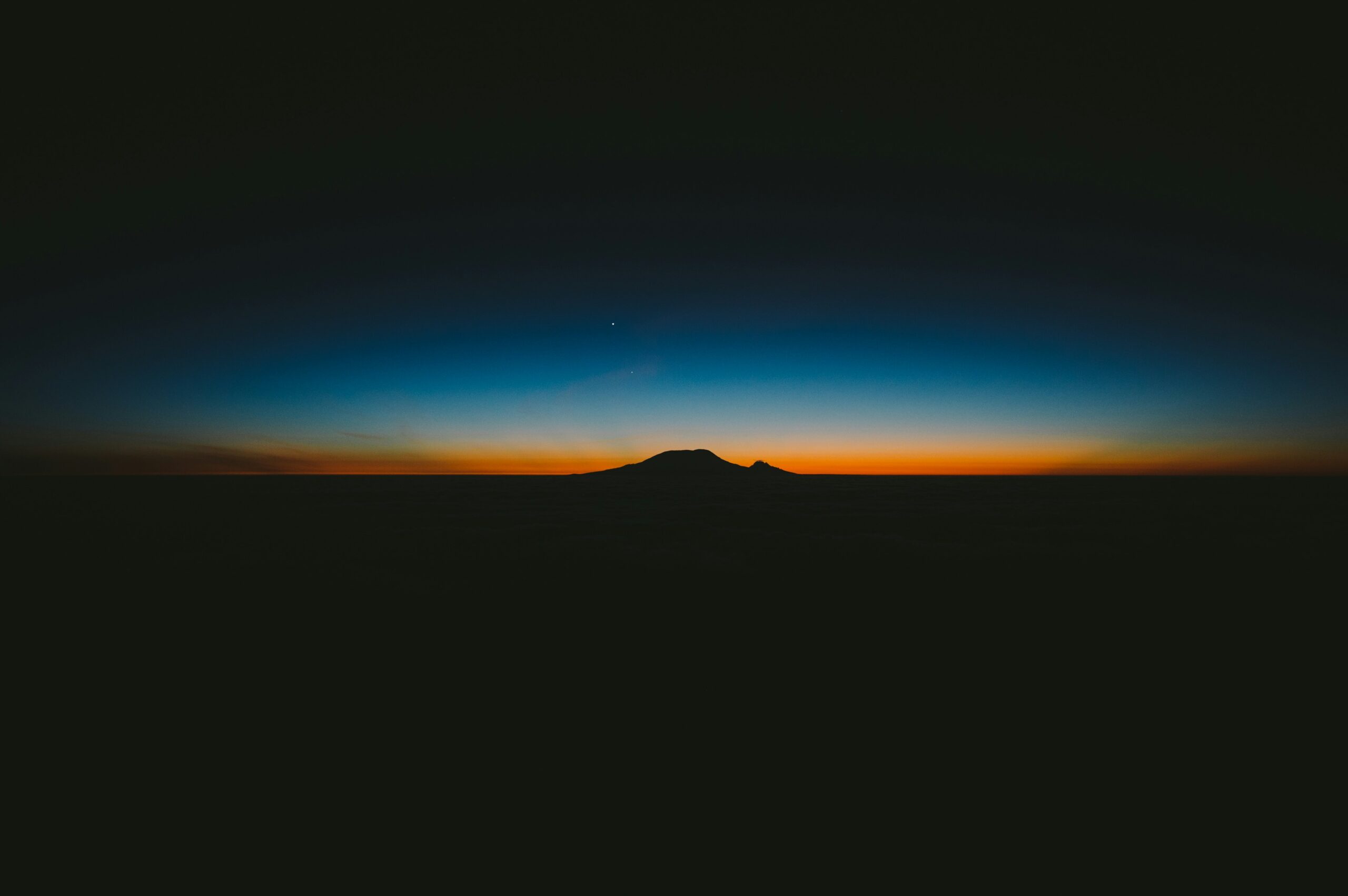 A picture of a silhouetted mountain as the sun is setting beautifully behind it.