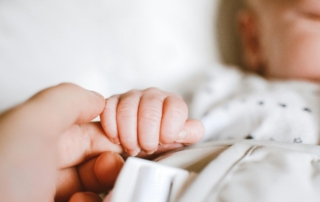 A heartwarming close-up photo of a baby’s hand gripping the finger of an adult.