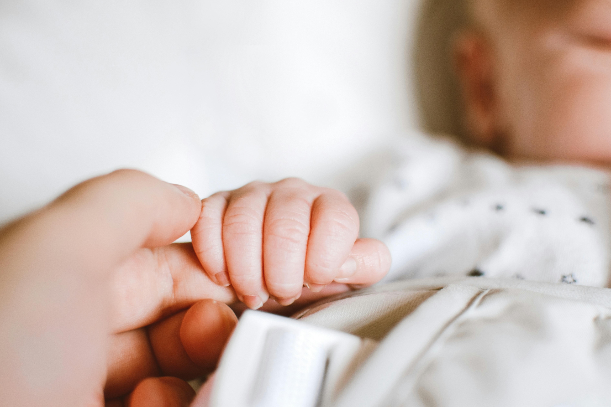 A heartwarming close-up photo of a baby’s hand gripping the finger of an adult.