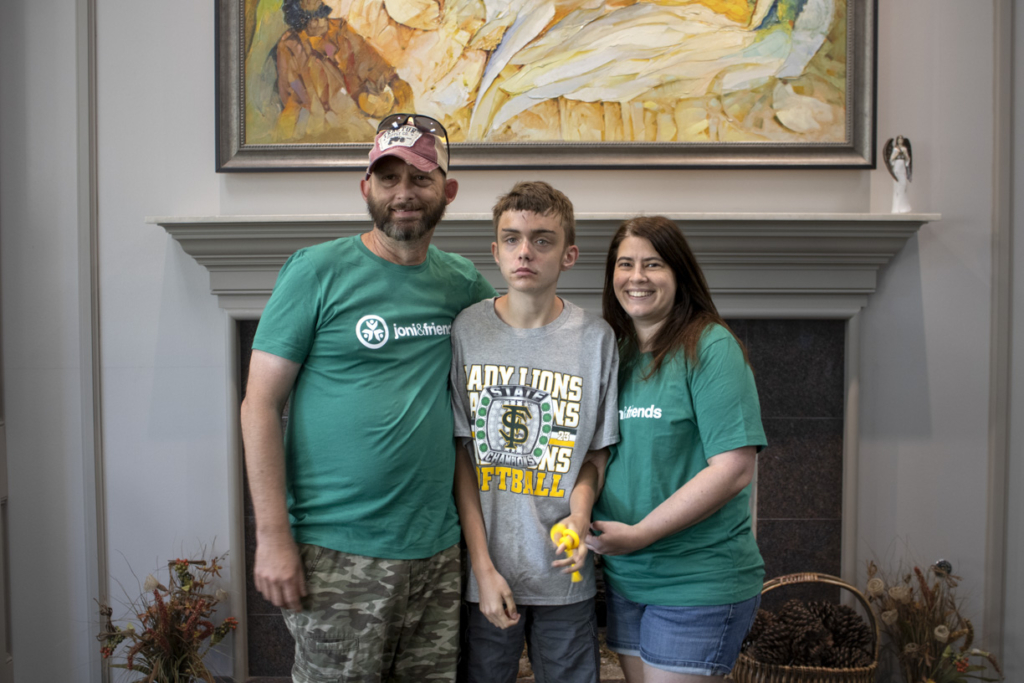 Adam on the left, Robbie in the middle, and Ashley on the right, smiling and posing for the camera at Family Retreat 2024. Behind them is a fireplace with a picture frame on top.