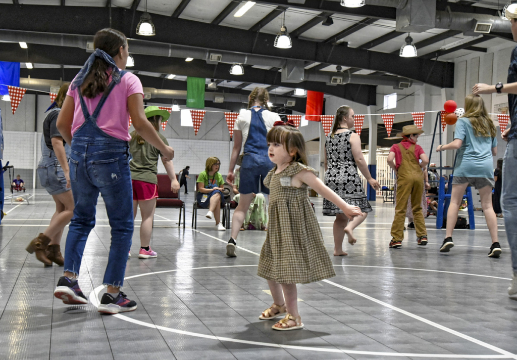 Natalie is dancing joyfully at the Barn Dance during the Missouri Family Retreat, surrounded by other people also dancing and having fun. The lively atmosphere captures a moment of celebration and community, with everyone enjoying the event together.