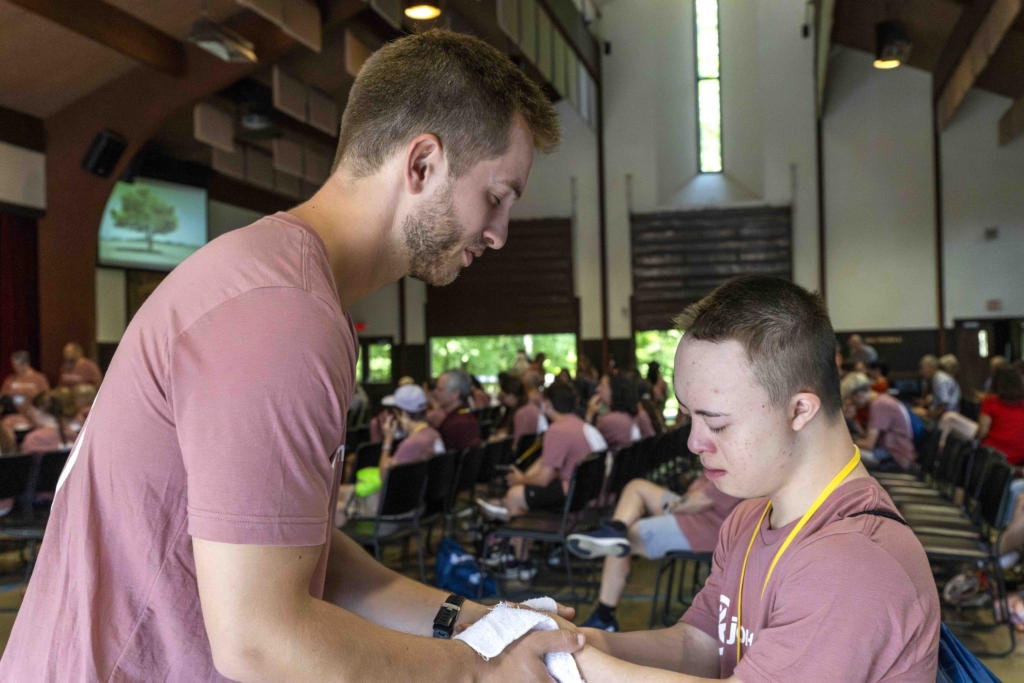 Josiah is holding hands with another volunteer at Joni & Friends, both with their eyes closed, praying together inside the church.