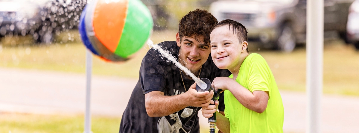 A volunteer and camper shooting water at a beach ball