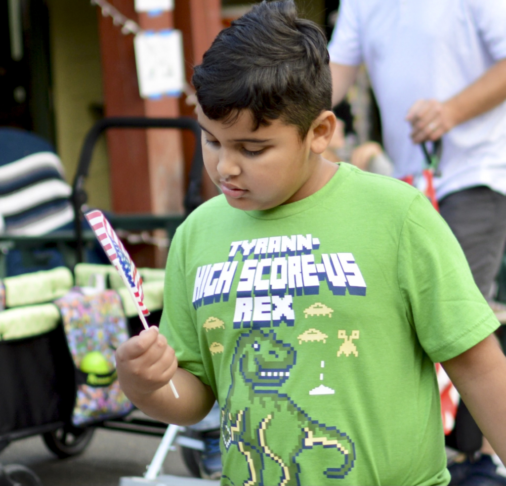 Oscar, wearing a green shirt, is looking intently at a small American flag. His focus is on the flag as he observes it closely.