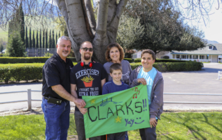 The Clark family standing and posing for the camera, holding a cloth with the word "CLARKS!!" written on it.