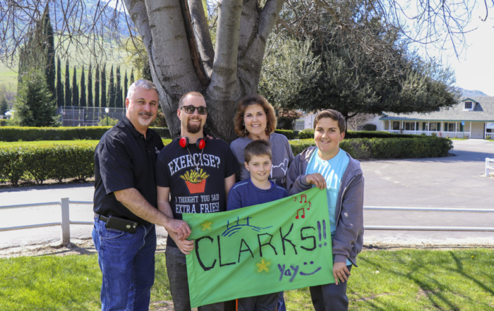 The Clark family standing and posing for the camera, holding a cloth with the word "CLARKS!!" written on it.