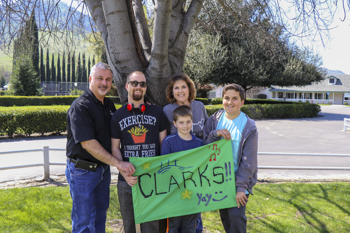 The Clark family standing and posing for the camera, holding a cloth with the word "CLARKS!!" written on it.