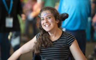 Jaycee smiles broadly during Family Retreat, with colorful butterfly face paint on her face.