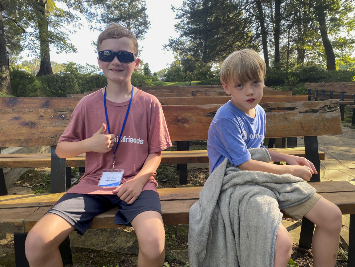 Elijah is sitting on a bench with his buddy at Family Retreat, smiling and enjoying the moment.