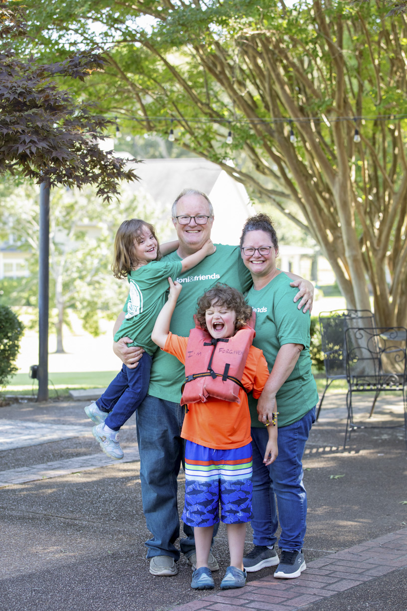 Chris, Lori, Elijah, and Chris carrying their daughter, all posing and smiling for the camera outdoors.