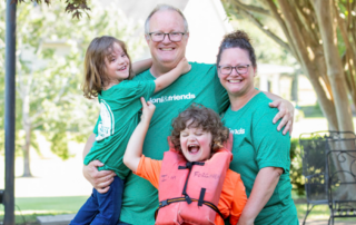 Chris, Lori, Elijah, and Chris carrying their daughter, all posing and smiling for the camera outdoors.