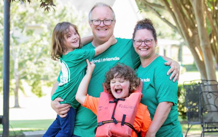 Chris, Lori, Elijah, and Chris carrying their daughter, all posing and smiling for the camera outdoors.