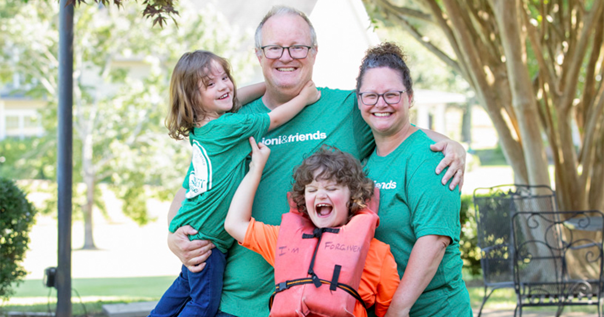 Chris, Lori, Elijah, and Chris carrying their daughter, all posing and smiling for the camera outdoors.