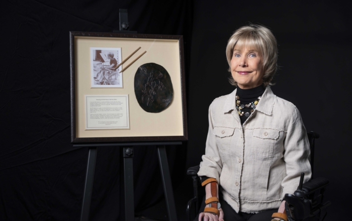 Joni next to her artwork Cowboy on a Bucking Horse. The art is a drawing of a cowboy riding a bucking bronco on a glazed-and-fired ceramic.