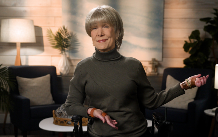 Joni wearing a turtle neck and smiling for the camera in a cozy living room setup.