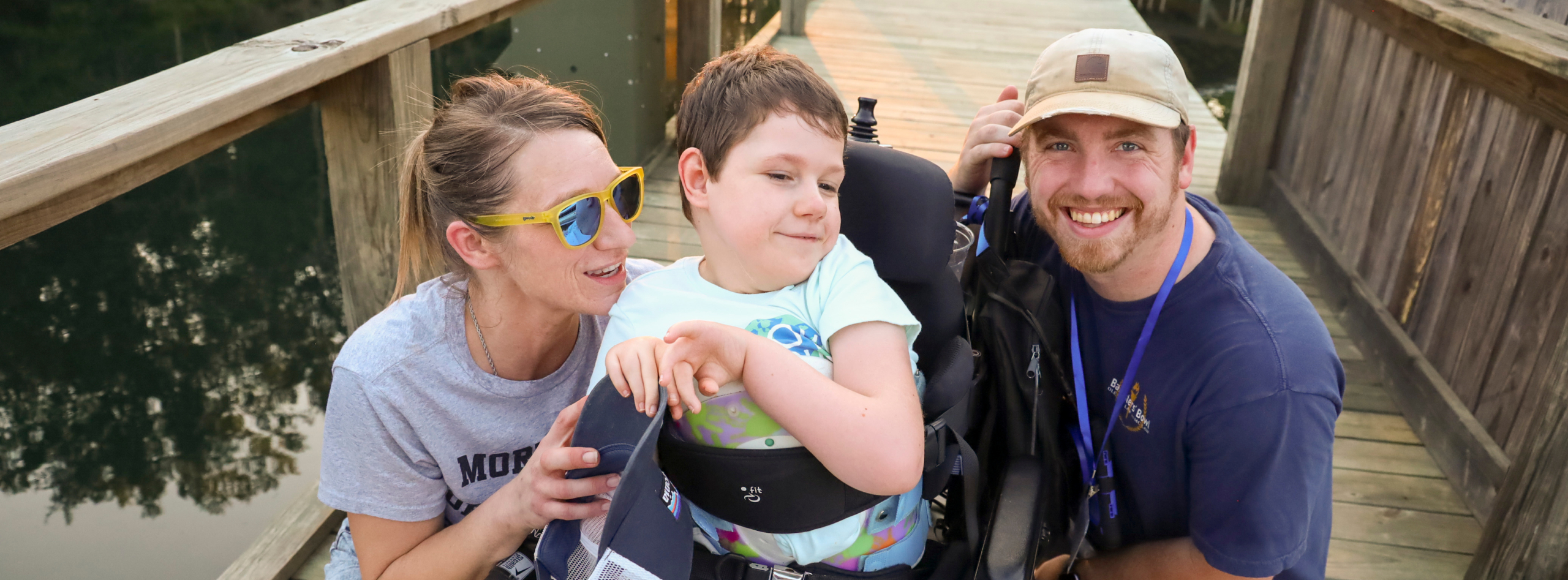 A boy in a wheelchair enjoying time with a man and a woman, all smiling and having fun at a Family Retreat.