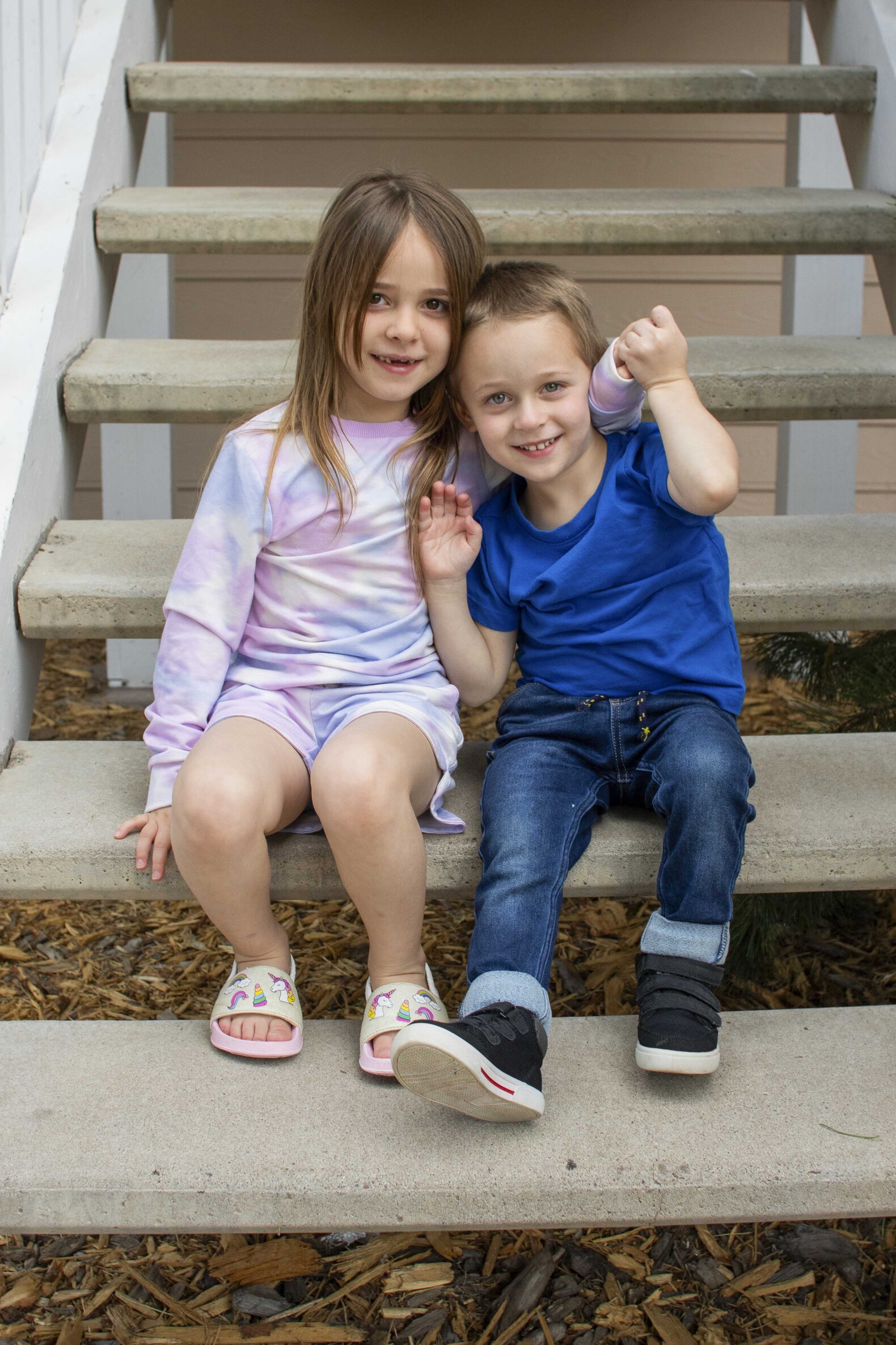 Isa and Isaiah sitting on the steps of the staircase, looking excited and happy while looking at the camera.