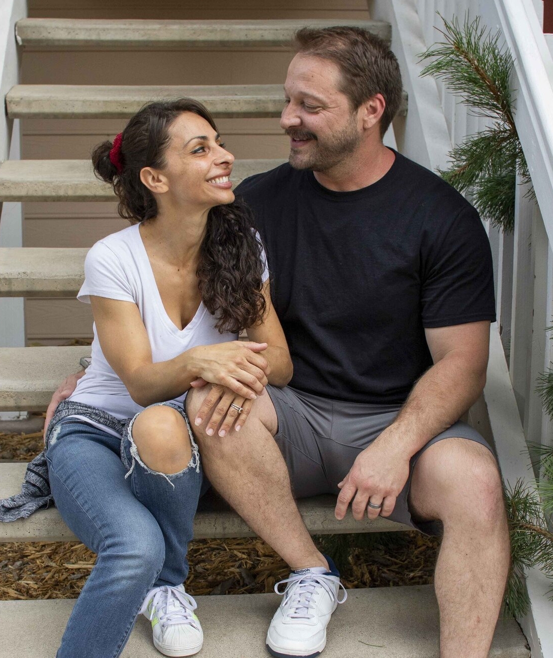 Lea and Gabriel looking at each other affectionately and smiling while sitting on the steps of a staircase.