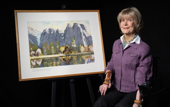 Joni next to her artwork "Yosemite Afternoon" featuring the majestic rock formations in Yosemite.
