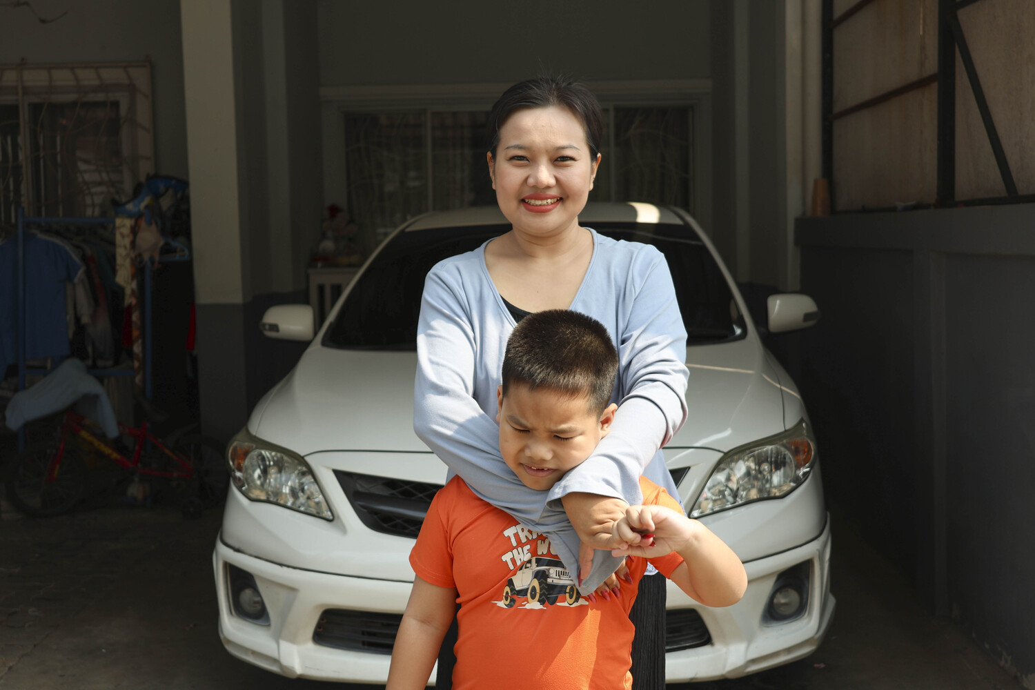 Praram standing with his mom, Phornnapa, behind him, hugging him and both smiling for the camera.